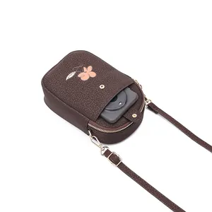 Détail montrant un smartphone dans la poche avant d'un sac bandoulière marron.
