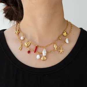 Macro detail of a gold stainless steel layered necklace with shell, pearl and starfish charms