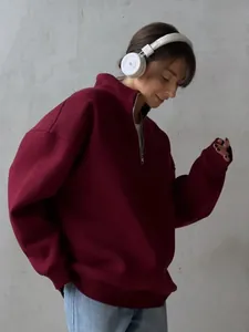 Close-up of a woman in a burgundy half-zip oversize sweatshirt with white headphones.