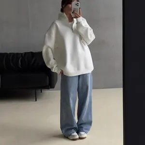 Woman wearing an oversized white half-zip fleece sweatshirt and light blue denim jeans