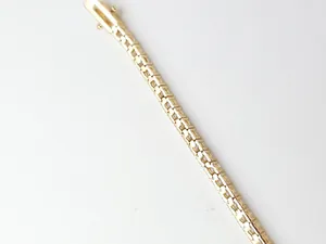 Primo piano di un bracciale tennis dorato a fila singola con pietre di zircone cubico.