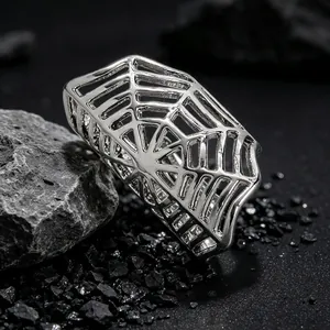 Close-up detail of a silver spider web ring presented on a textured black stone background