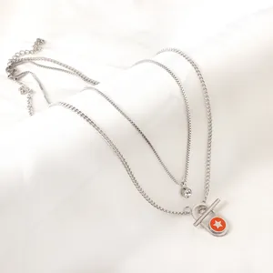 Nahaufnahme einer Edelstahlkette mit orangefarbenem Sternanhänger und T-Verschluss.