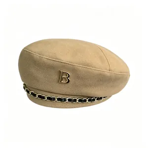 Detailansicht einer khakifarbenen Wollbaskenmütze mit goldenem B-Logo und Kette