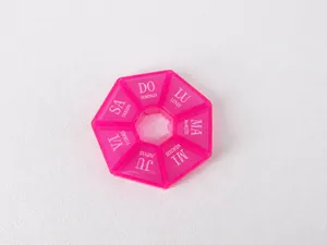 Vue de dessus d'un pilulier hebdomadaire rose rouge à 7 compartiments sur fond blanc