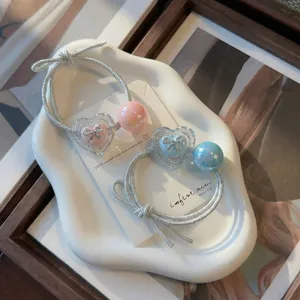 Close-up of heart-shaped bow hair ties with iridescent beads on a white ceramic tray.