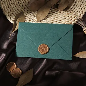 Detail view of dark green linen envelope with vintage gold wax seal and dried leaves