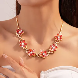 Close-up detail of vintage gold chain necklace featuring red rhinestone flowers worn on neck