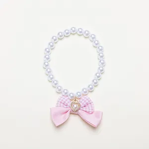 Close-up view of a pet pearl necklace featuring a pink gingham bow and heart charm
