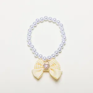 Close-up detail of a pearl pet collar featuring a yellow gingham bow and heart charm