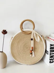Sac à main rond en paille tressée minimaliste avec poignée ronde et ruban de dentelle.