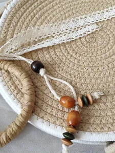 Détail du sac en paille rond avec ruban en dentelle et pompon en perles