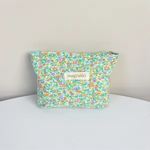 Macro view of floral canvas makeup bag featuring a 'mayrabbit' brand label and zipper