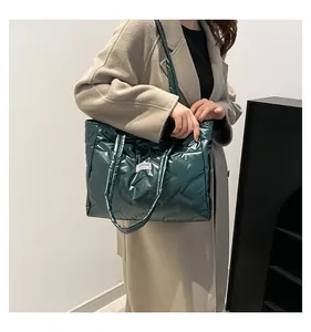 Metallic green down-filled quilted tote bag carried by a model in a beige coat