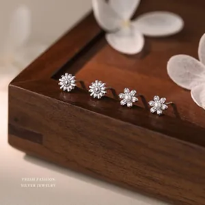 Close-up of four delicate silver daisy stud earrings displayed on a dark wooden box