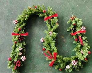 Detail van een feestelijke kerstslinger met rode ornamenten en bessen op groene takken.