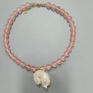 Detailweergave van een roze kralenketting met een witte natuurlijke schelphanger.