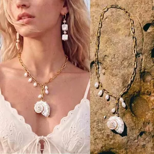 Gedetailleerd beeld van een gouden schakelketting met een schelphanger en druppelvormige parels.