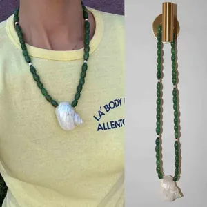 Detailweergave van een handgemaakte groene kralenketting met een natuurlijke witte schelphanger.