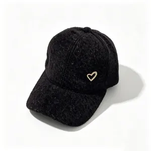 Detail of a black fuzzy baseball cap featuring a golden rhinestone heart embellishment.