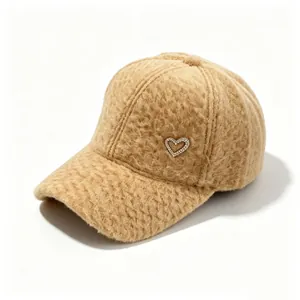 Detail view of a fuzzy beige alpaca wool baseball cap with rhinestone heart emblem.