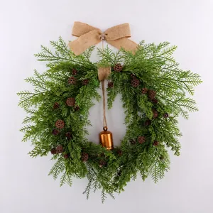 Front view of Christmas wreath featuring pine cones, a rustic bell, and a burlap bow.