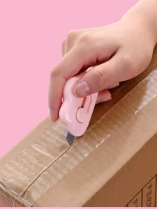 Close-up view of a pink cloud-shaped mini utility knife cutting through a cardboard box.
