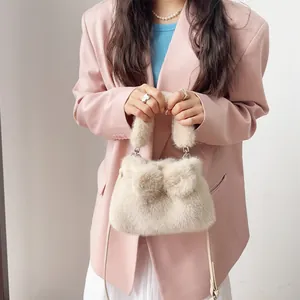Nahaufnahme einer cremefarbenen Kunstpelz-Handtasche mit Bommel-Schleifen und Outfit.