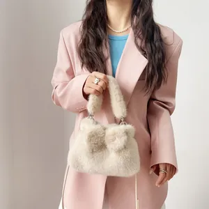 Modell hält eine flauschige beige Kunstpelz-Handtasche mit Schleife vor rosa Blazer