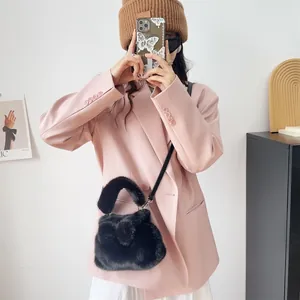 Model trägt eine schwarze flauschige Kunstpelz-Handtasche mit Schleife zu einem rosa Blazer.