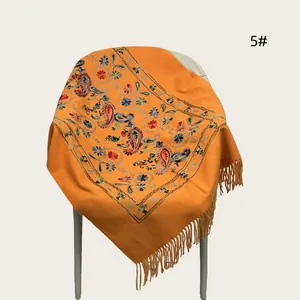Orange embroidered shawl with paisley patterns and tassels draped on a white chair.