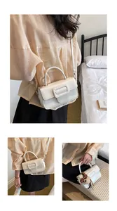 Gros plan d'un petit sac carré en cuir ciré crème avec poignée et boucle décorative.