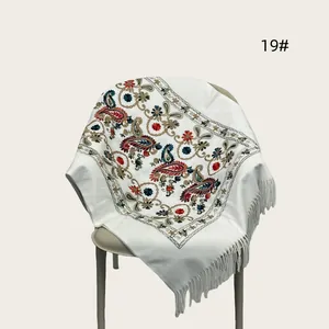 Detailed view of white embroidered shawl with paisley patterns and elegant tassels