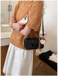 Vue détaillée d'un petit sac carré noir en cuir huilé avec breloque en peluche et sangle