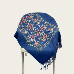 Blue embroidered shawl with floral patterns and tassels draped on a white chair