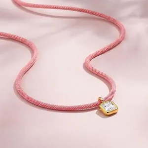 Primer plano de un collar de cordón rosa con colgante cuadrado de circón dorado brillante.