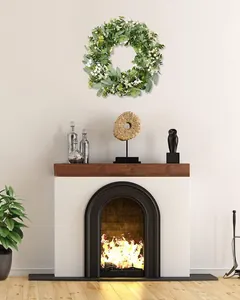 Artificial eucalyptus and white berry wreath hanging above a cozy white fireplace
