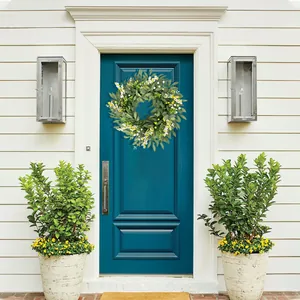 Artificial eucalyptus and berry wreath hanging on a blue front door in a garden setting
