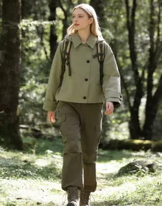 Female model walking in a forest wearing a sage green hooded cloak-style windbreaker jacket.