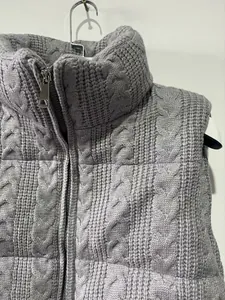 Detailed view of a gray cable-knit puffer vest featuring a high neck and silver metal zipper.