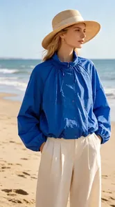 Full view of blue nylon jacket featuring stand collar and pleated neck details on beach.