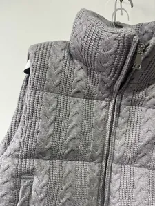 Close-up of grey cable-knit padded vest with zipper detail and high collar.