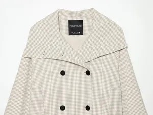 Detail einer karierten Jacke mit breitem, überlappendem Kragen und schwarzen Doppelknöpfen.