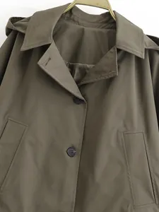 Detailed view of hooded collar and button closure on an olive green cape-style trench coat