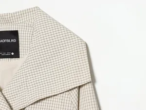 Detailansicht einer karierten Oversized-Jacke mit schwarzem Marken-Etikett am Hals.