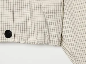 Detailaufnahme eines schwarzen Knopfes und Gummisaums an einer beige karierten Jacke