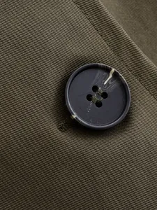 Close-up of a marbled button and olive green twill fabric on a stylish hooded windbreaker jacket