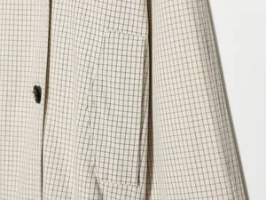 Nahaufnahme einer cremefarbenen Karojacke, die Stoffstruktur und Pattentasche zeigt
