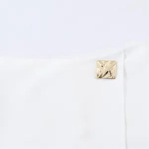 Macro view of white asymmetric skort featuring a textured square golden button detail