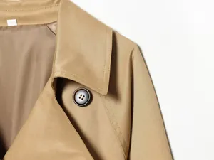 Detalle en primer plano de la solapa y el botón de una gabardina corta beige mujer.